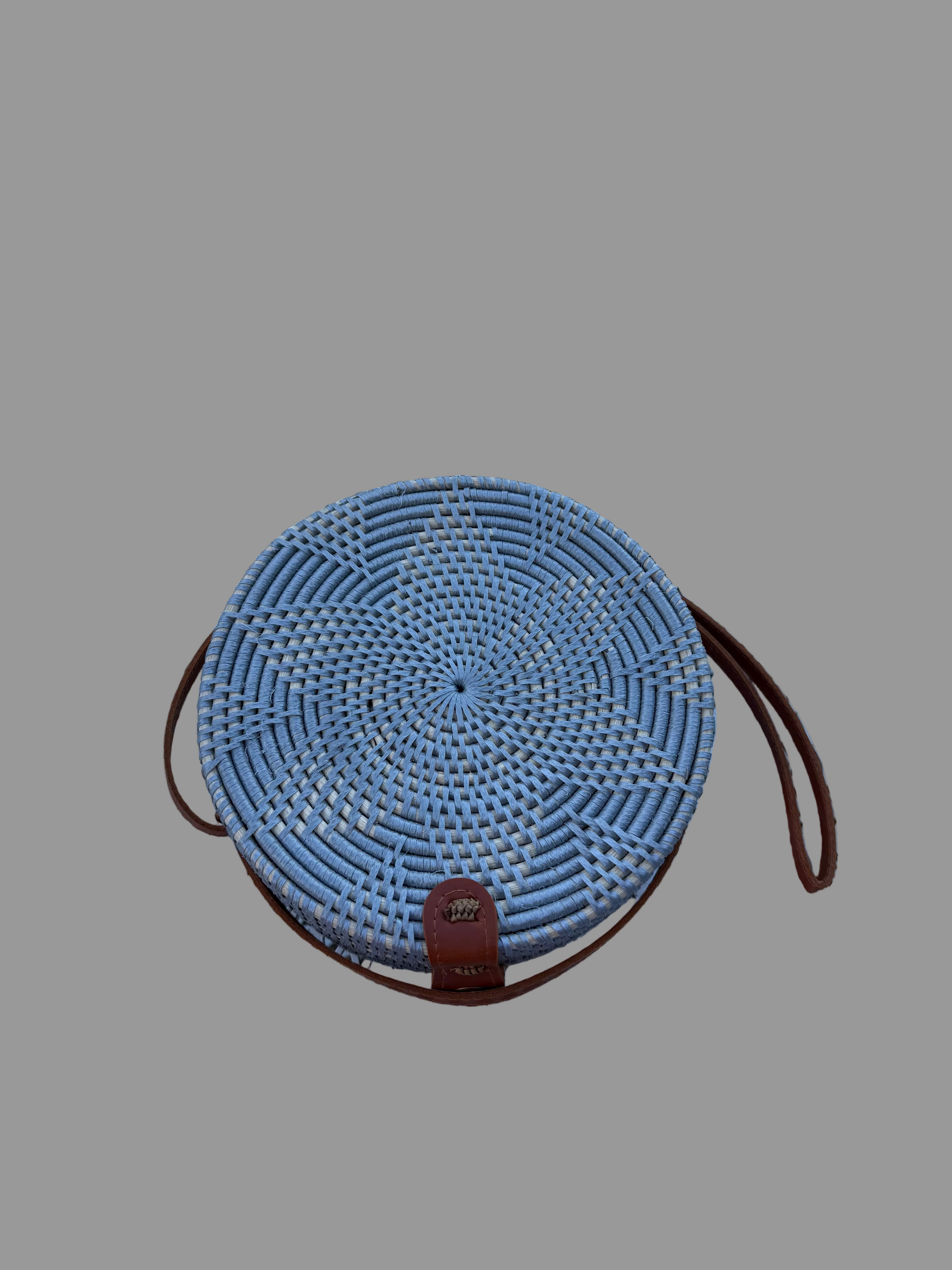 Round woven basket with a brown strap on a textured white surface